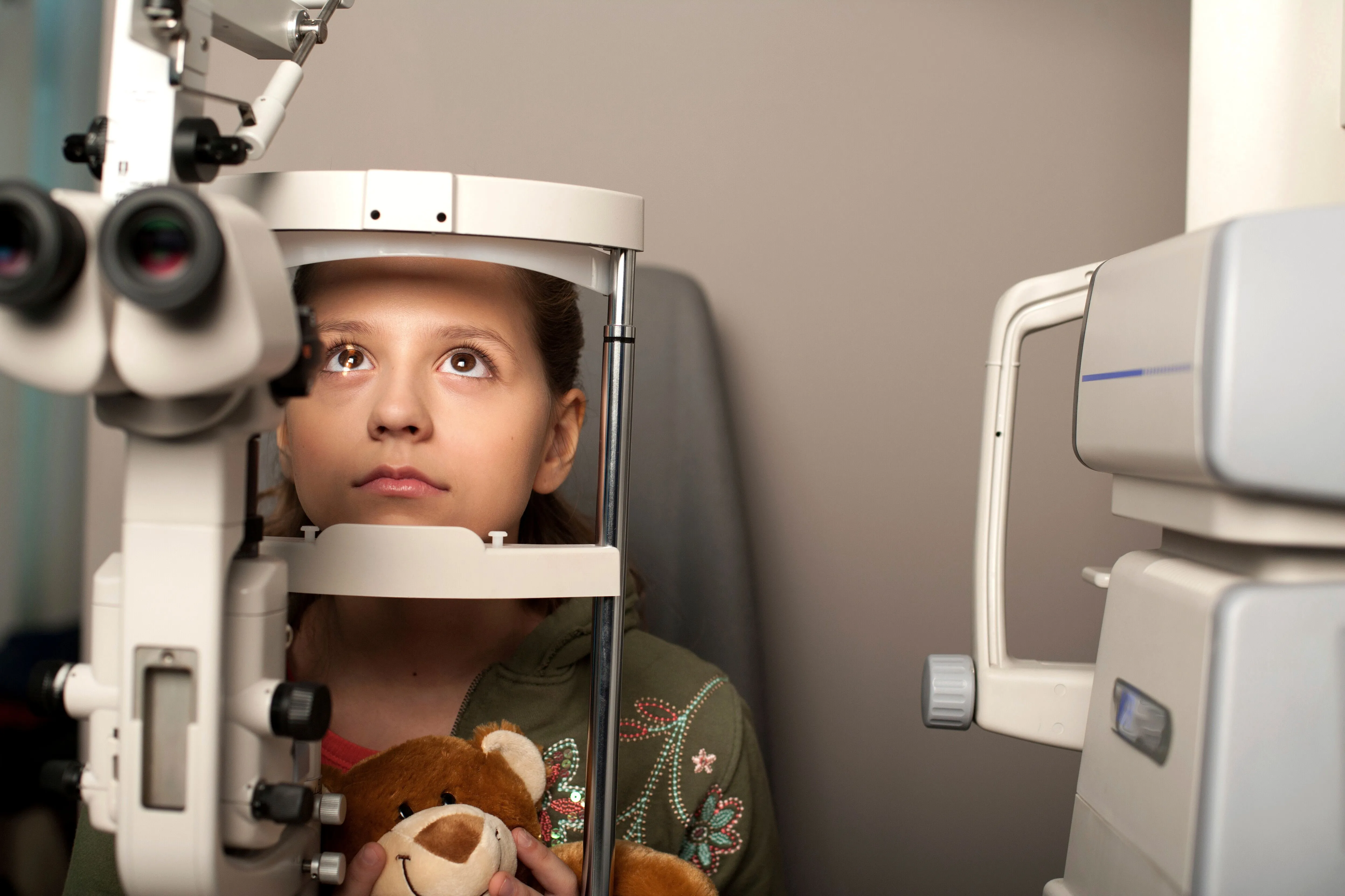 A girl is having an eye exam and we see her resting her chin on an eye care diagnostic tool.