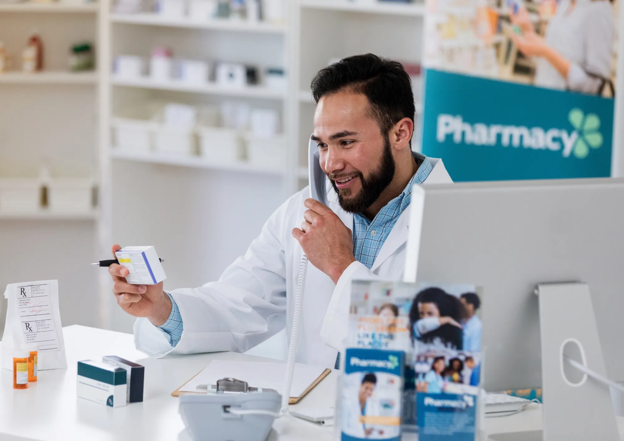 A pharmacist holds a prescription while on the phone in a pharmacy.