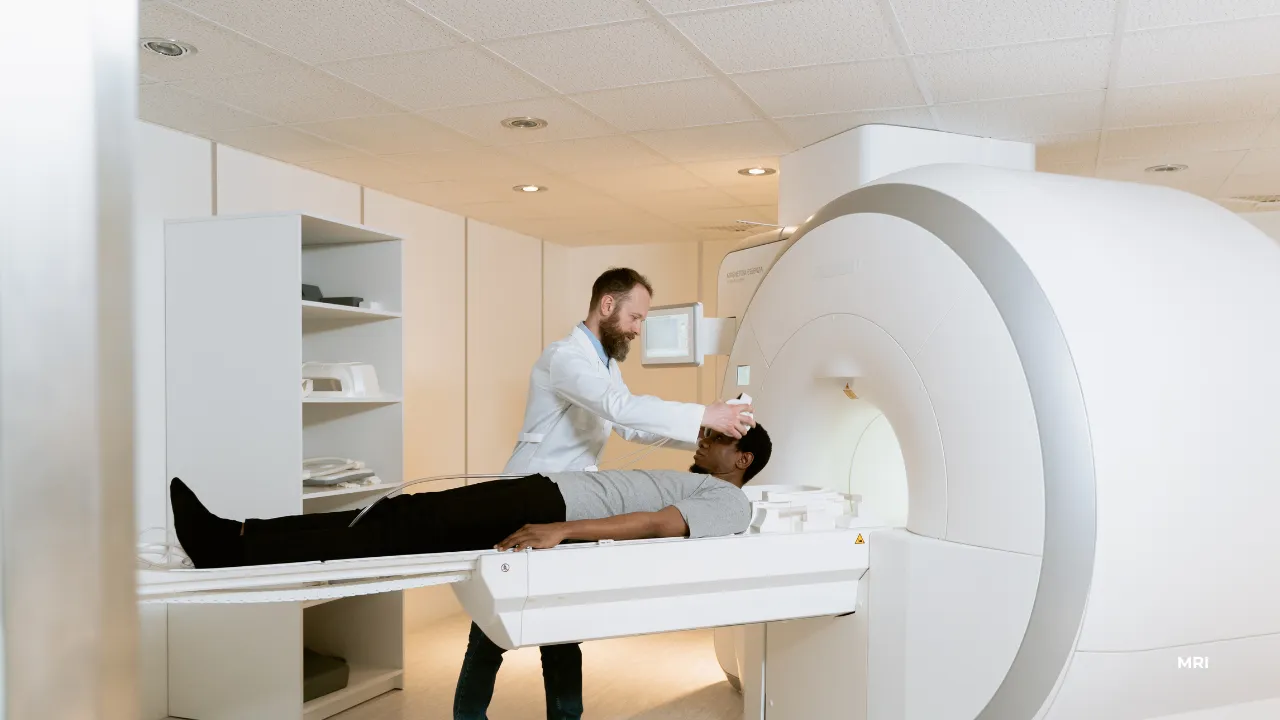 A MRI patient lays on an MRI bed with a medical professional overseeing.