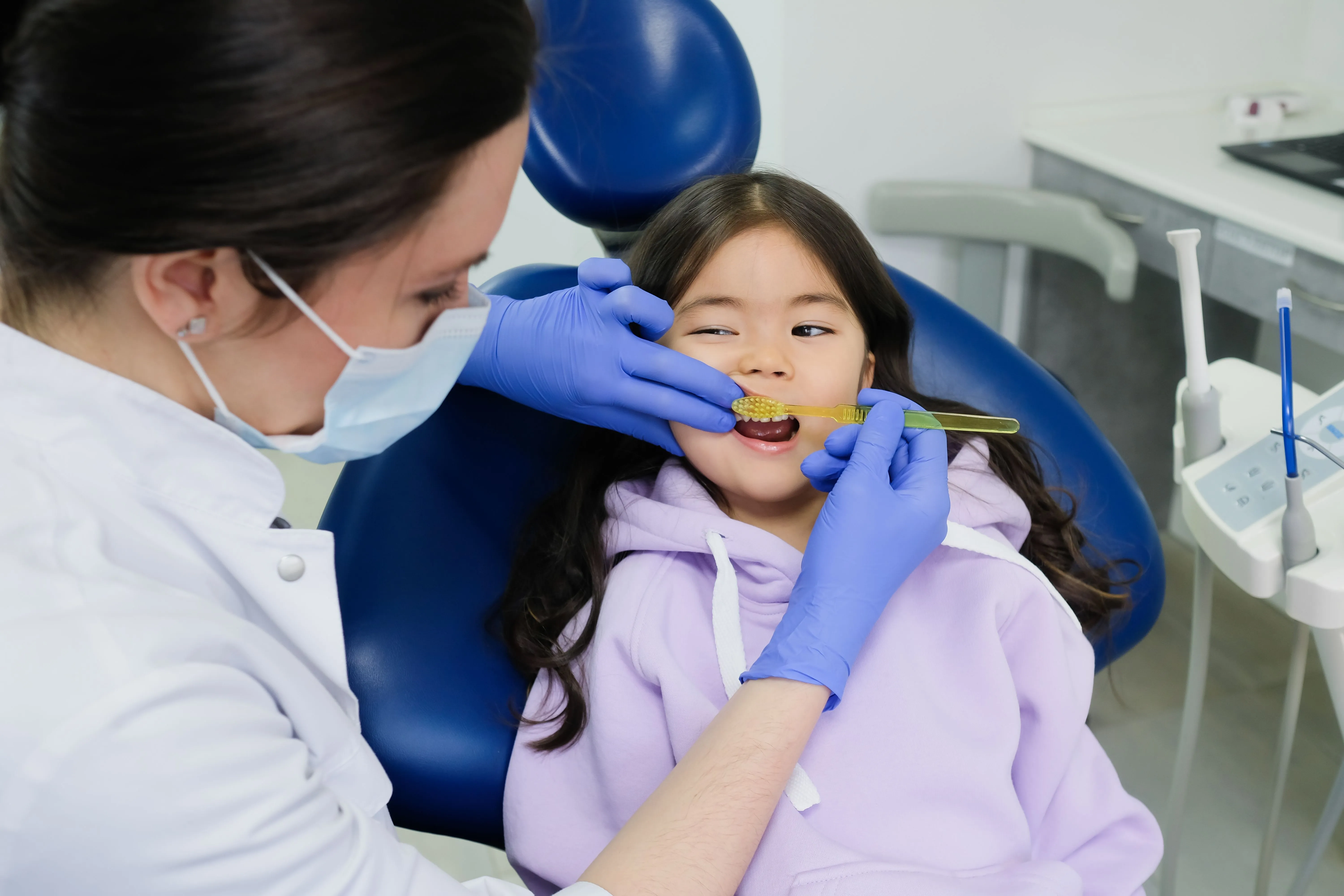 A dentist cleans the teeth of a young girl.